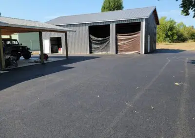 Metal garage with two open bays covered by tarps beside covered vehicle port