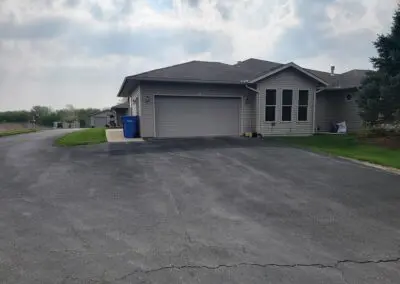 Suburban garage front with driveway, trash bin, lawn, and cloudy sky