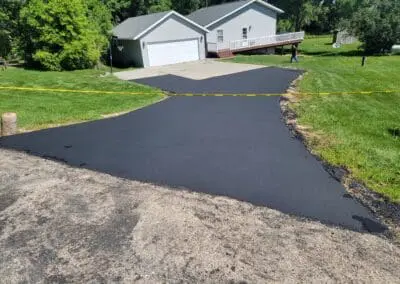 Newly sealed black asphalt driveway leading to suburban garage and house