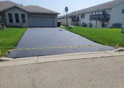 Newly sealed residential driveway with caution tape in front of garage