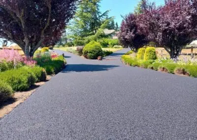 Freshly paved residential driveway lined with flowering beds and trees