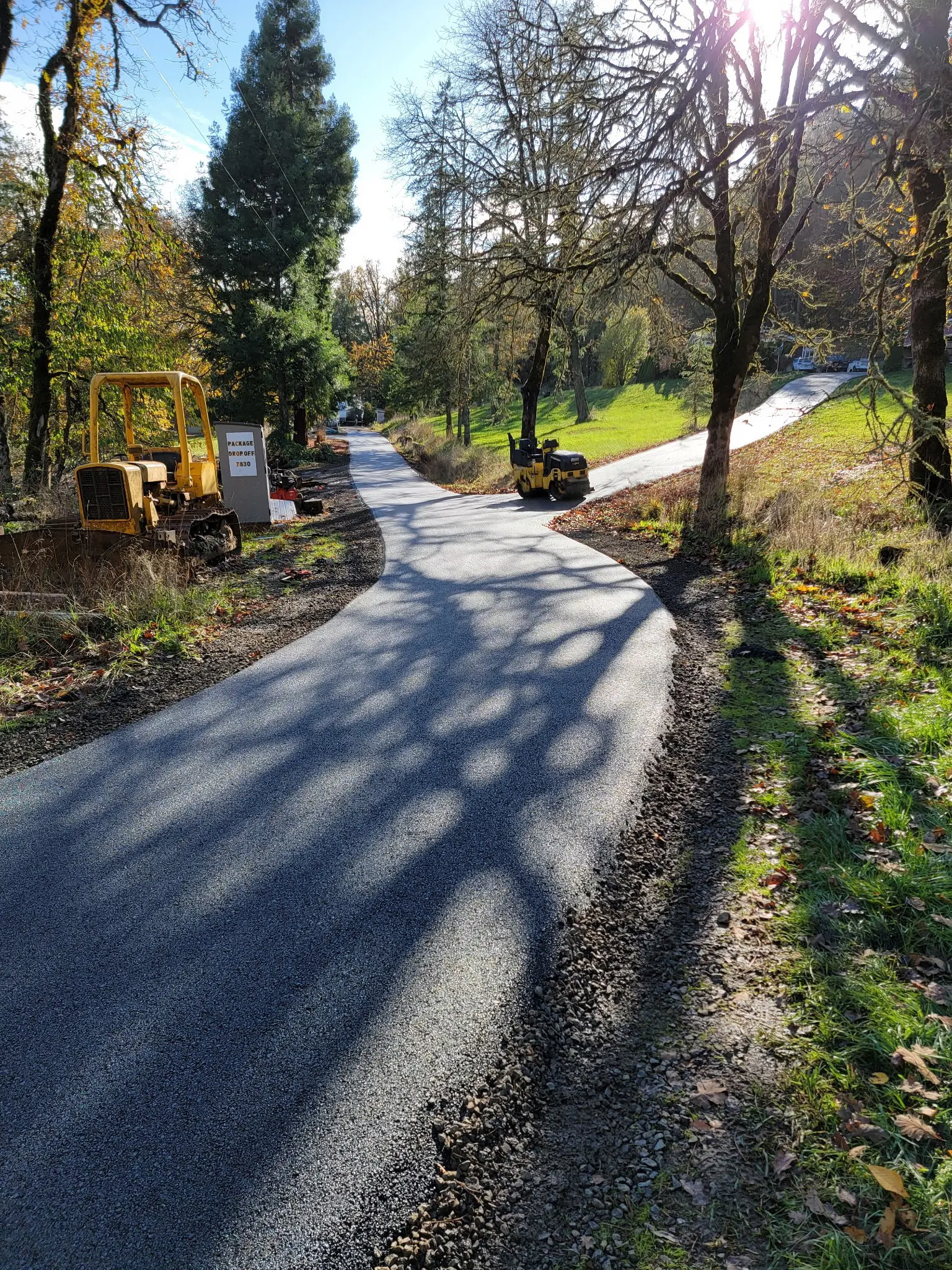 Newly paved driveway winding through trees with asphalt roller and equipment