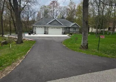 Freshly sealcoated driveway leading to three-car garage, caution tape visible