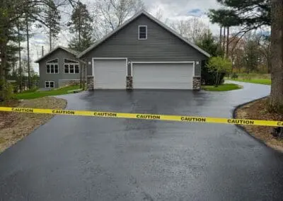 Freshly sealcoated driveway leading to three-car garage, caution tape visible